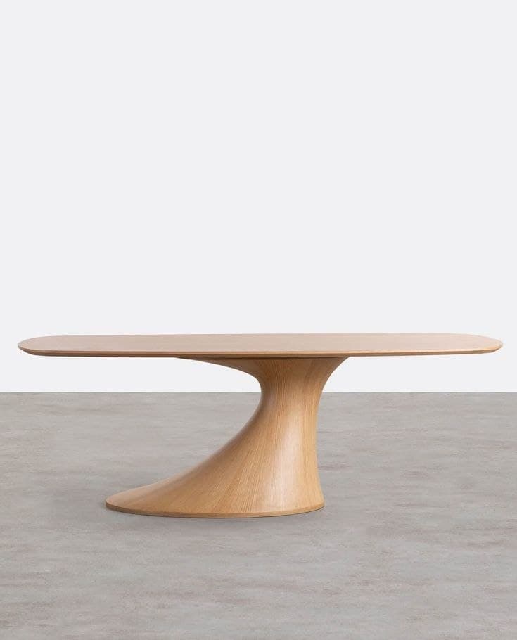 Low-slung fluid oval coffee table with a beautifully flared curving pedestal base in a warm light-oak wood grain texture, standing on a minimalist grey concrete floor